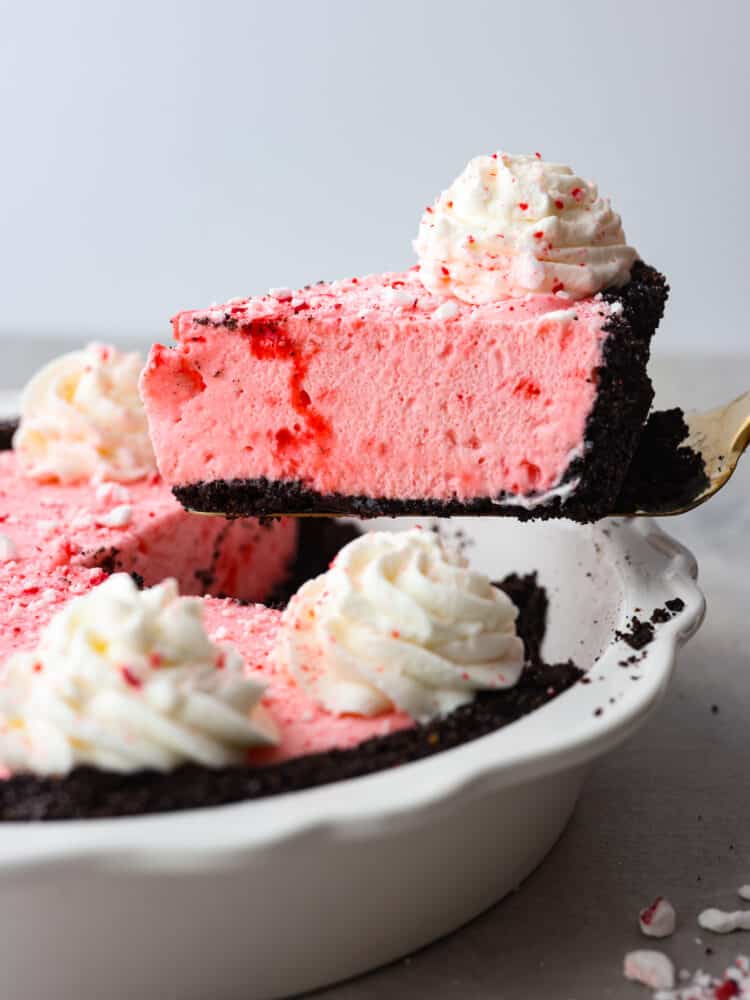 If you are looking for the perfect holiday dessert, then this is it! This Oreo Crust Peppermint Pie has all of the flavors that you want to serve your guests throughout the season. It's creamy and delicious, and you won't be able to stop at one slice! A slice of peppermint pie being served out of the pie dish with a gold pie server.