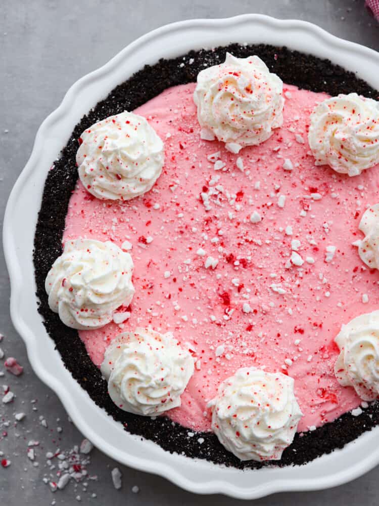 If you are looking for the perfect holiday dessert, then this is it! This Oreo Crust Peppermint Pie has all of the flavors that you want to serve your guests throughout the season. It's creamy and delicious, and you won't be able to stop at one slice! The top view of an order crust peppermint pie. garnished with dollops of whipped cream and crushed peppermint.