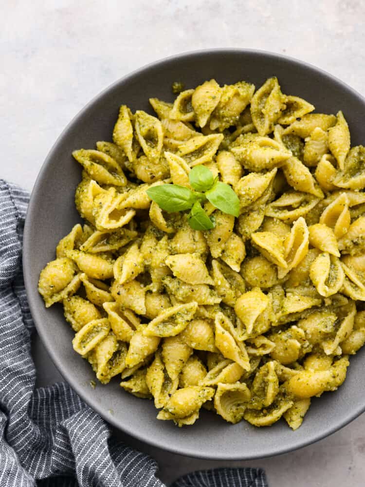 10-minute pesto pasta is made with fresh basil, parmesan, pine nuts, and olive oil. It brings incredible flavor to your pasta dish and is ready in no time at all!ย Top-down view of pesto pasta served in a gray bowl, garnished with herbs.