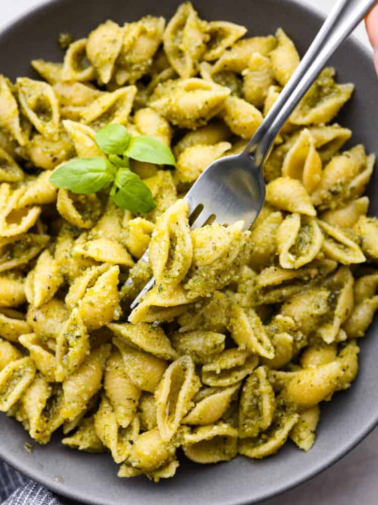 10-minute pesto pasta is made with fresh basil, parmesan, pine nuts, and olive oil. It brings incredible flavor to your pasta dish and is ready in no time at all!ย Closeup of a fork skewering multiple shell-shaped noodles.