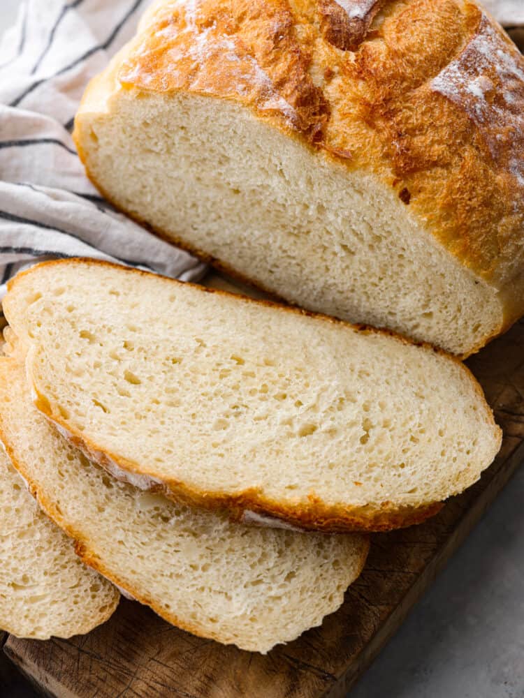 Potato bread is a soft white bread that is spongy and delicious. The potatoes add a fluffy yet firm texture making it perfect for sandwiches, toast, or warmed with jam. Close up view of sliced pieces of bread on a rustic brown cutting board. Half of the loaf is sliced, and the other half of the loaf is still whole.