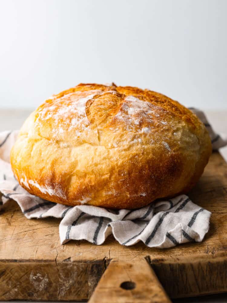 Potato bread is a soft white bread made with mashed potatoes. The potatoes add a fluffy texture making it incredibly delicious. Side view of a loaf of potato bread on top of a striped kitchen towel and rustic cutting board.