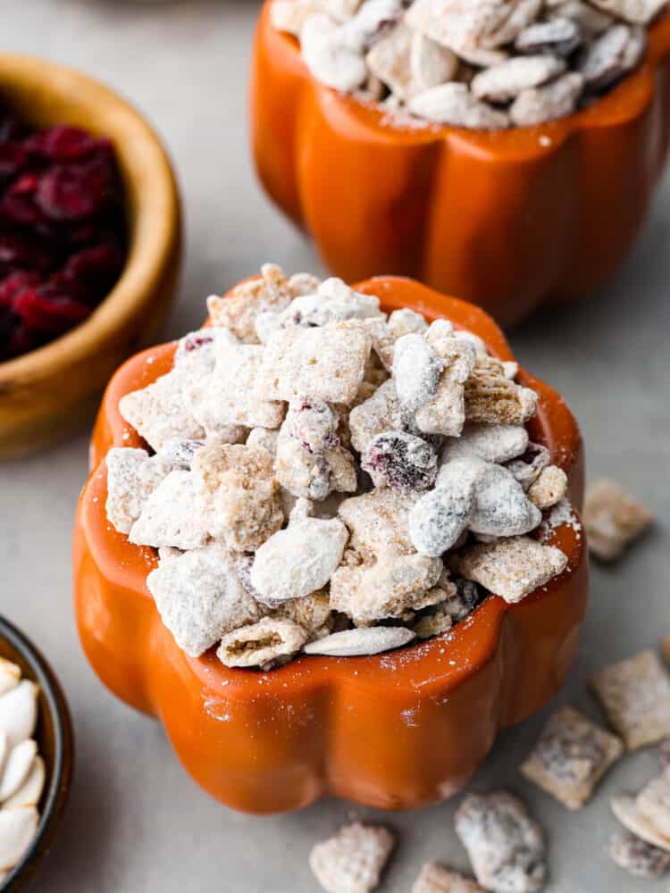 Prepare yourself for the best fall treat around- delicious pumpkin spice combined with one of the easiest treats on the planet - muddy buddies! The crunchy Chex Mix, chocolate, powdered sugar, and added cranberry and fall spices will make you want to finish the whole bowl. Closeup of pumpkin spice buddies in a pumpkin-shaped jar.