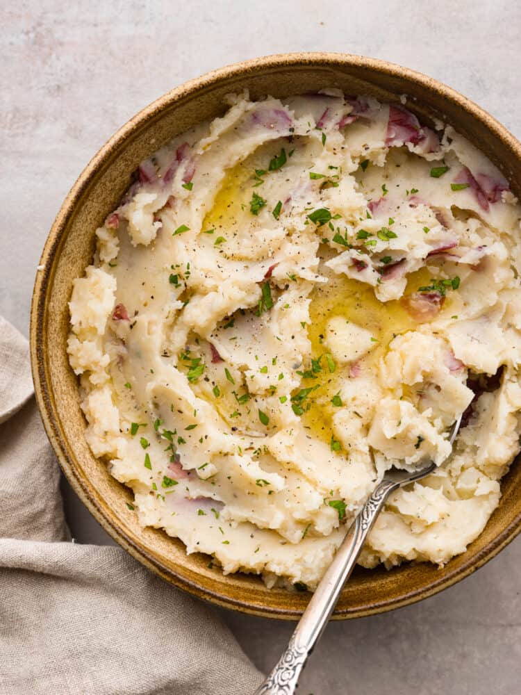 These Instant Pot mashed potatoes are an easy side dish for any holiday or weeknight dinner! They are creamy and flavorful and come together in just 15 minutes. Mashed potatoes served in a brown bowl. There is a silver spoon in the bowl of potatoes.