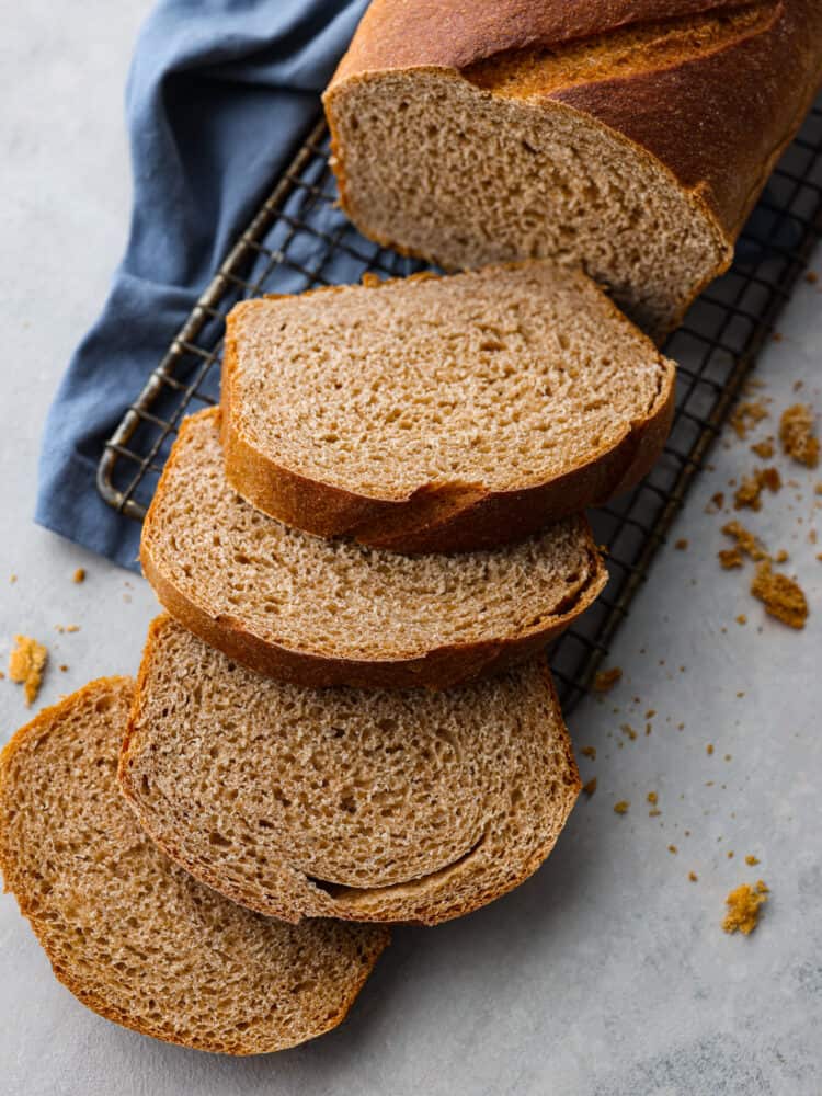 This Sprouted Wheat Bread is fluffy, moist, and full of rich flavor! If you are a skeptic of whole wheat bread because you've tried store-bought in the past, get ready to change your mind! I promise even picky eaters love the nutty flavor and soft texture of this homemade bread. Sliced Sprouted Whole Wheat bread on a cooling rack with a blue tea towel underneath.