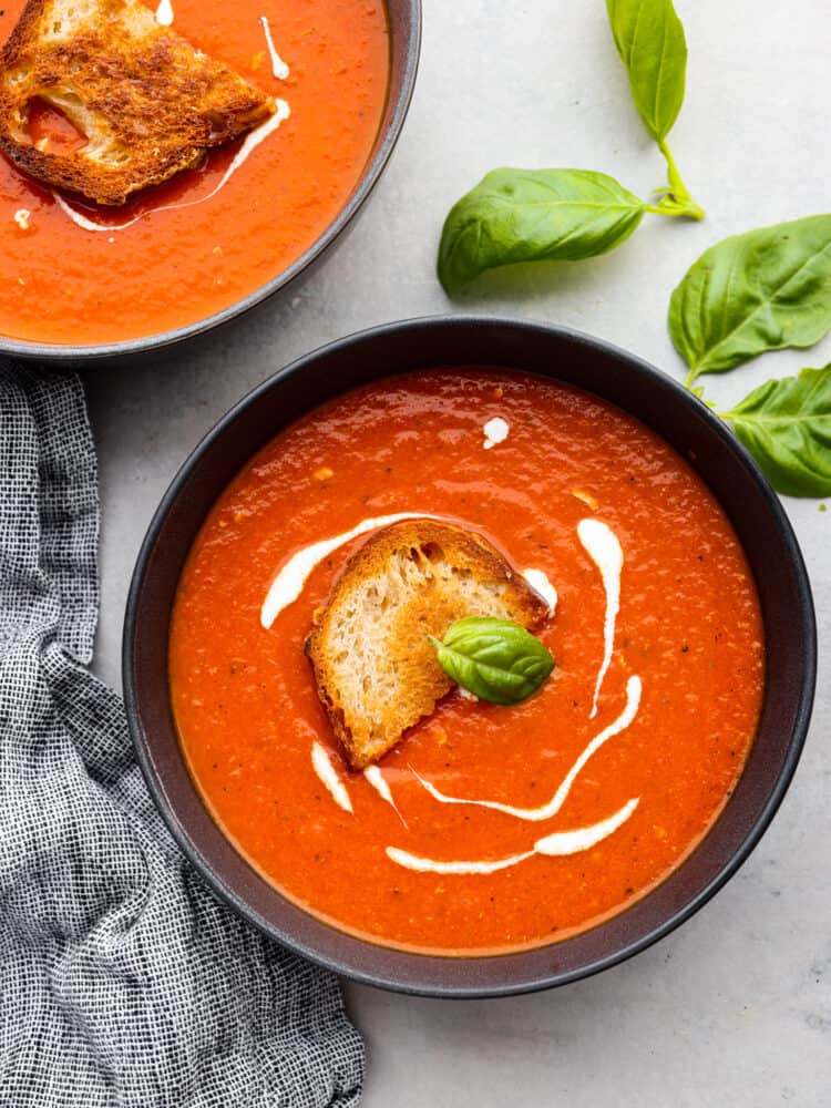 Tomato basil soup is a healthy classic that's simple to make from scratch and full of flavor! It only takes just over half an hour. The whole family will enjoy it as the temperatures drop and the evenings become crisper. Two black bowls filled with soup.