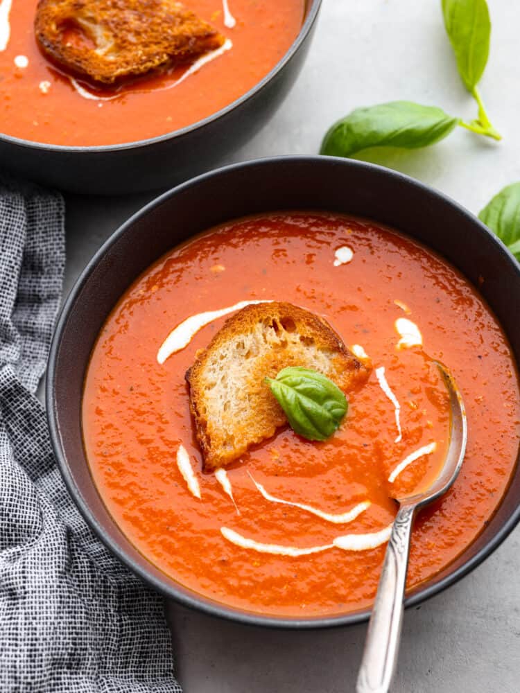 Tomato basil soup is a healthy classic that's simple to make from scratch and full of flavor! It only takes just over half an hour. The whole family will enjoy it as the temperatures drop and the evenings become crisper. Top-down view of tomato basil soup, drizzled with cream and served with bread.