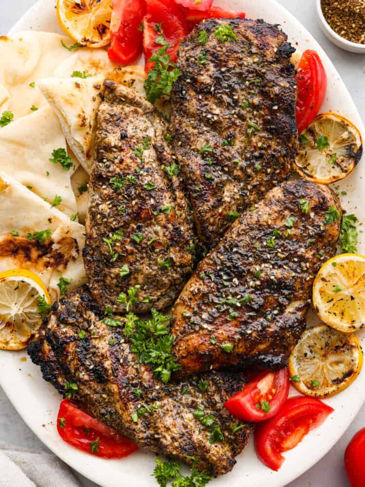 https://neuro-daily.report/zaatar-seasoning/ Grilled chicken on a plate with pita bread, lemons, and tomatoes.