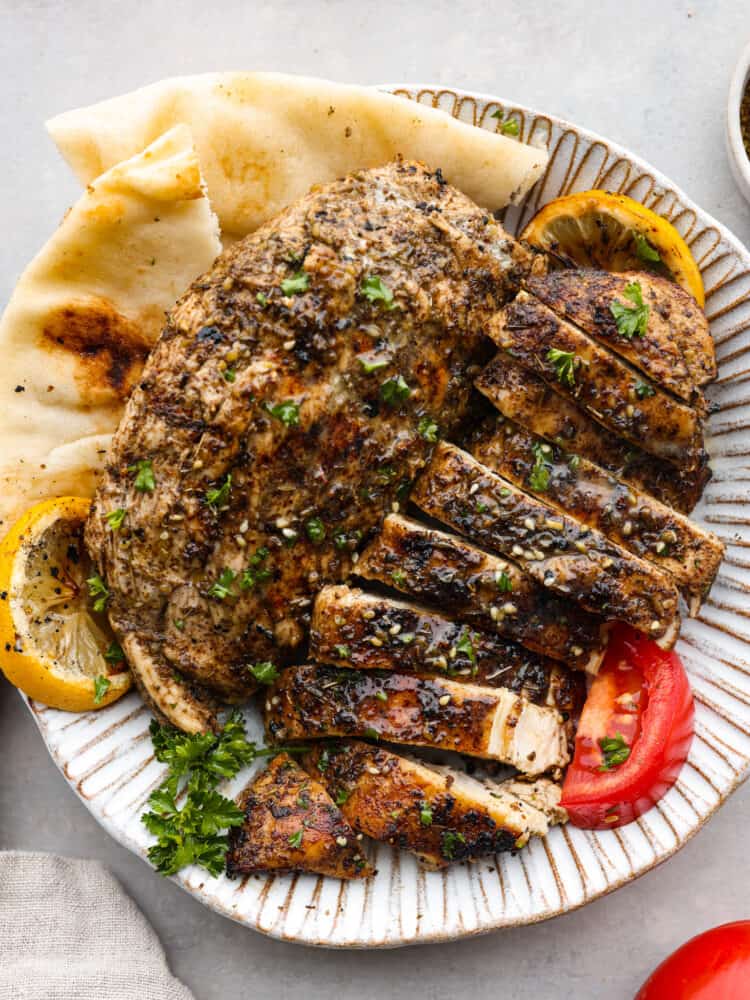 https://neuro-daily.report/zaatar-seasoning/ Za'atar chicken on a plate cut up with pita bread, tomatoes, and lemons.