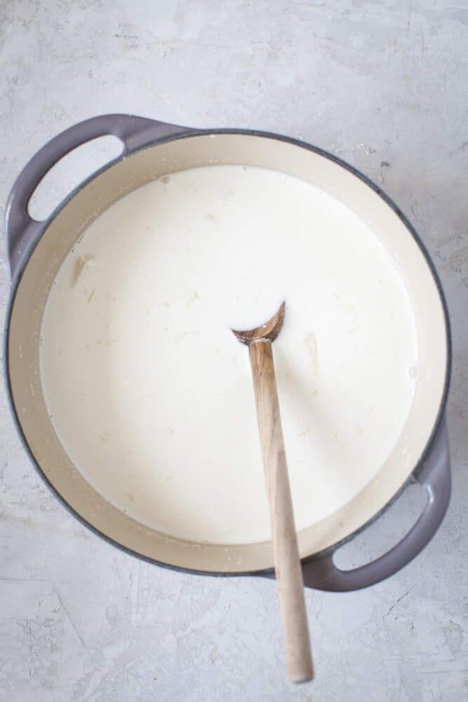 White Hot Chocolate is a rich and creamy decadent drink that melts in your mouth with a smooth, sweet white chocolate and vanilla flavoring. Warm up with this delicious hot chocolate throughout the entire holiday season! White hot chocolate in a pot with a wooden spoon.