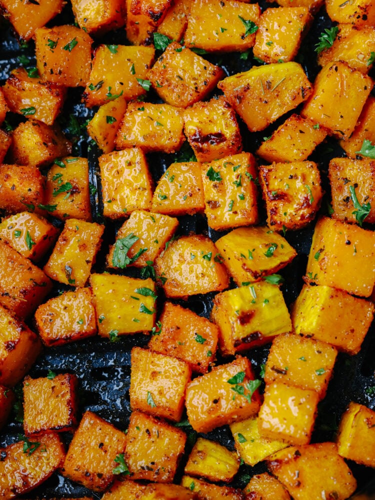 This easy air fryer butternut squash is tender and savory and makes the BEST side dish to any meal! Seasoned with delicious spices the air fryer cooks this squash to perfection. Close up view of air fryer butternut squash garnished with fresh parsley.