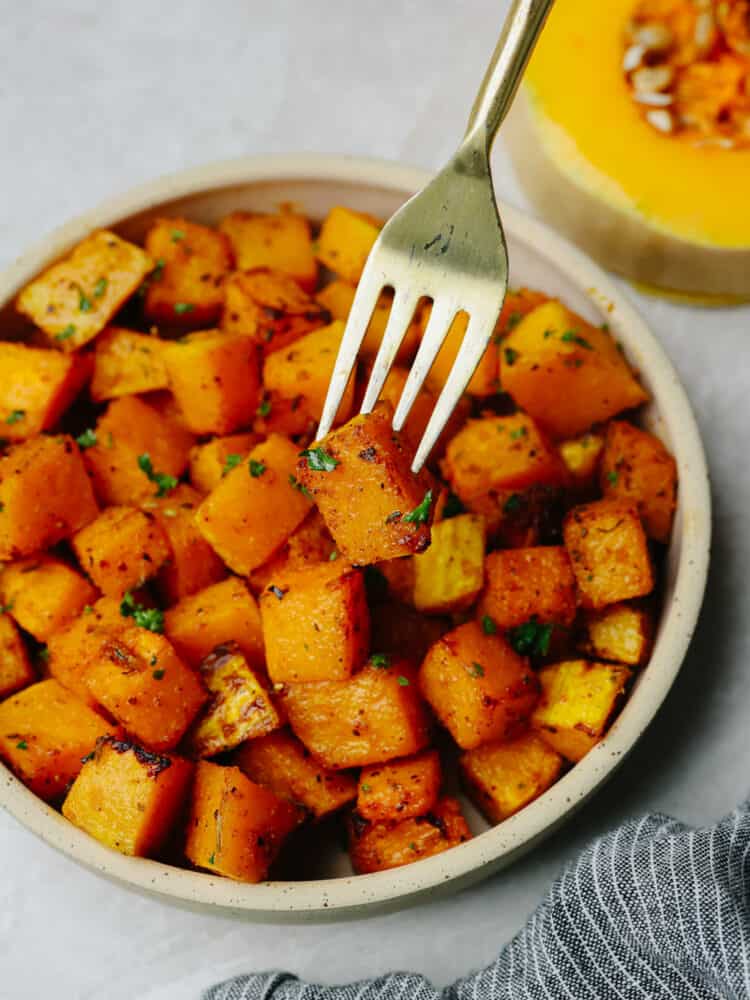 This easy air fryer butternut squash is tender and savory and makes the BEST side dish to any meal! Seasoned with delicious spices the air fryer cooks this squash to perfection. Close up photo of squash on a small tan colored plate with a fork lifting out a piece of squash.