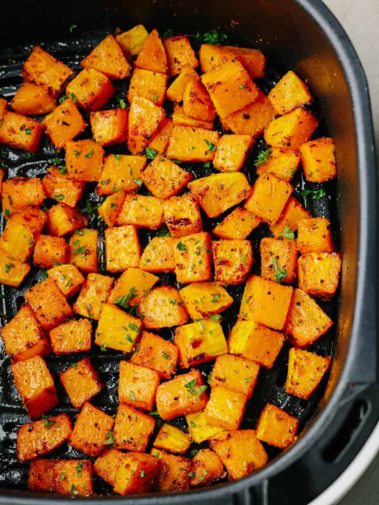 This easy air fryer butternut squash is tender and savory and makes the BEST side dish to any meal! Seasoned with delicious spices the air fryer cooks this squash to perfection. Top view of butternut squash in the air fryer and garnished with fresh chopped parsley.