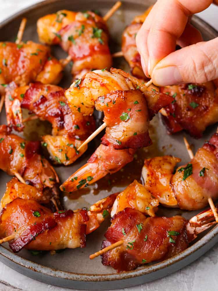 Bacon-wrapped shrimp coated in a sweet and savory glaze and broiled to perfection. The perfect easy appetizer or main course! Picking up a piece of shrimp wrapped in bacon.