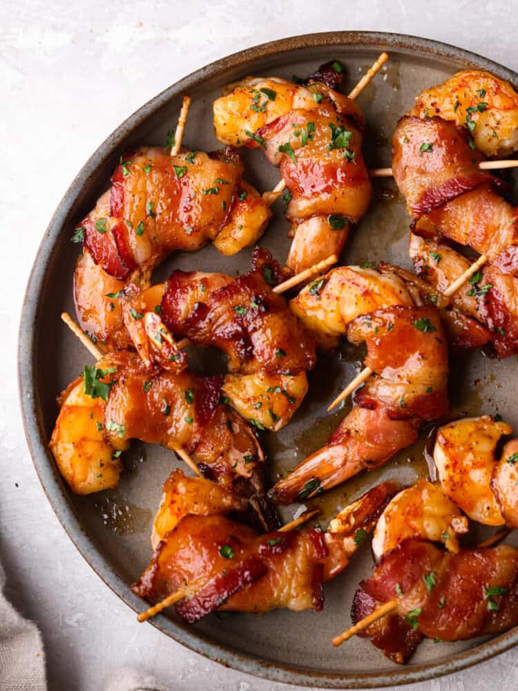 Bacon-wrapped shrimp coated in a sweet and savory glaze and broiled to perfection. The perfect easy appetizer or main course! Top-down view of bacon wrapped shrimp served on a gray plate.