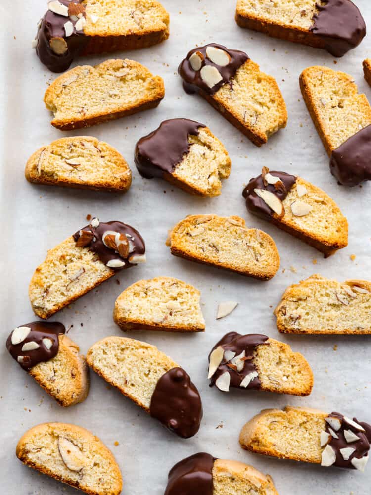 These Classic Biscotti are crispy and crunchy and melt in your mouth with a little help from some hot cocoa or coffee. Dipped in dark chocolate and sprinkled with sliced almonds, this fun treat is perfect for sharing with friends on a cold day! Finished classic biscotti sitting on parchment paper.