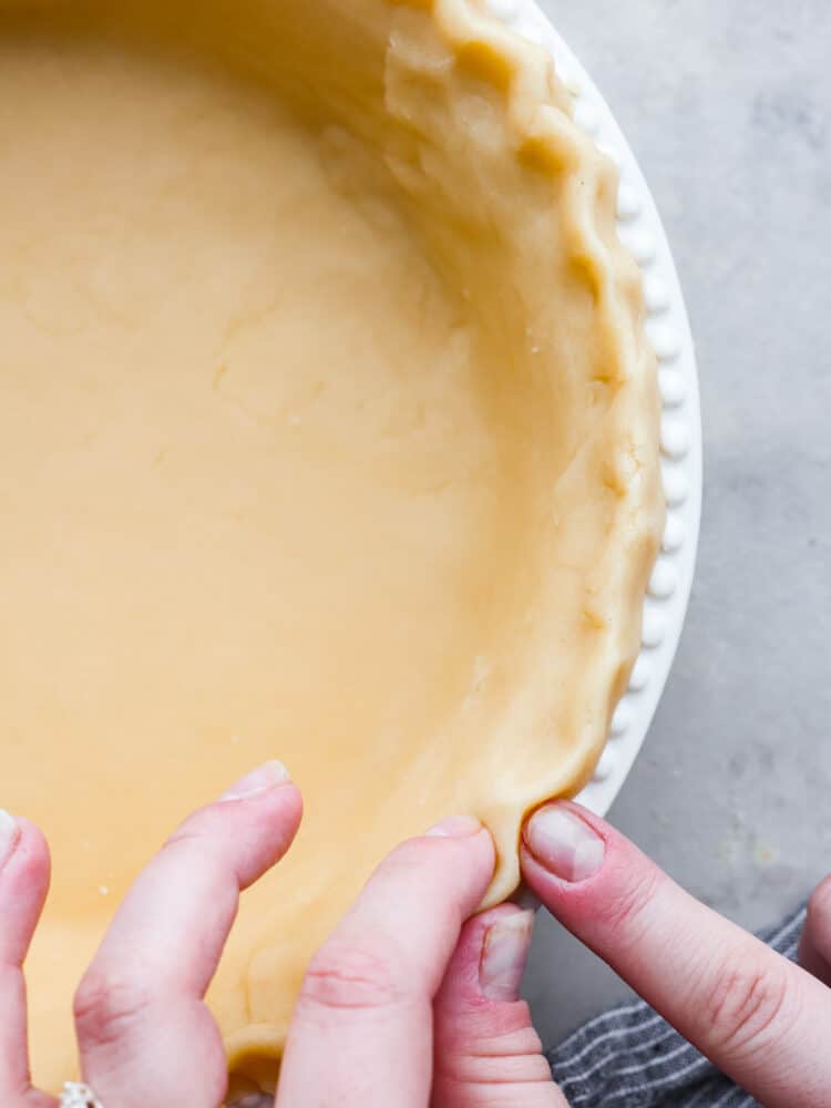 This Butter Pie Crust is the most tender and flaky crust you'll ever make! It's made from just four ingredients and will make the perfect base for all of your pies this holiday season. Close up of pie crust with hands crimping the edges.