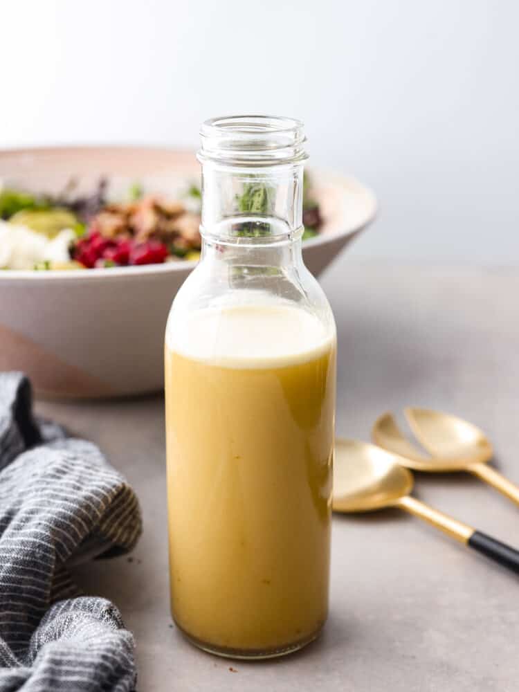 Champagne vinaigrette is a simple and elegant way to finish off any salad. It is tangy and sweet, and the champagne vinegar and orange juice adds the perfect flavor to your meal. It comes together in just 5 minutes and lasts a month in the fridge! Champagne vinaigrette in a glass jar with a salad in the background.