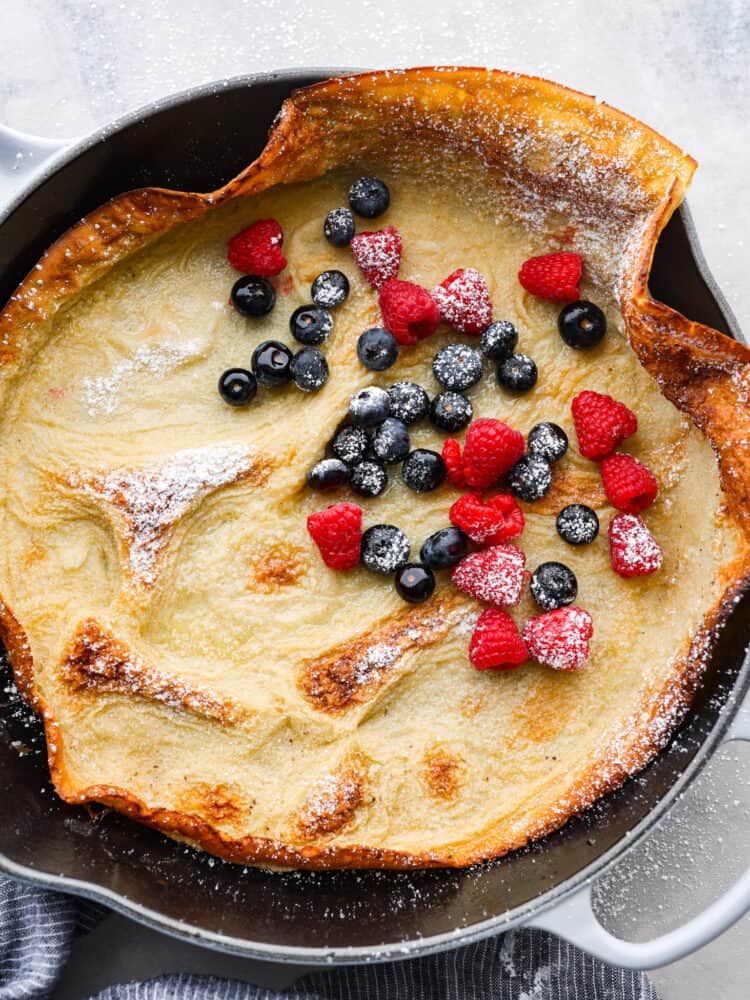 Light, fluffy, and deliciously oversized, this Dutch baby pancake is sure to please at the breakfast table! Add all of your favorite pancake toppings for a tasty treat the whole family will go crazy over. Top-down view of a Dutch baby in a cast iron skillet, garnished with powdered sugar and berries.