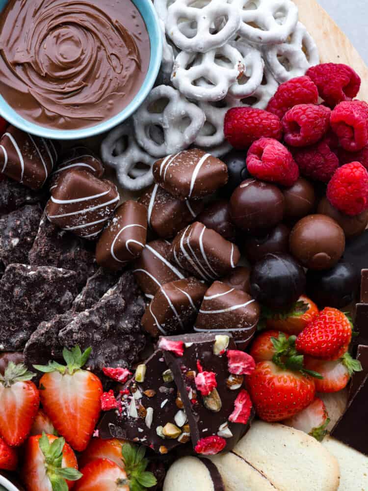 This chocolate charcuterie board is a chocolate lover's dream! Enjoy a chocolatey assortment of cookies, truffles, chocolate-covered pretzels, and fruit, along with decadent sauces for dipping! Top view of chocolate board with candy, pretzels, fruit, and a bowl of nutella.