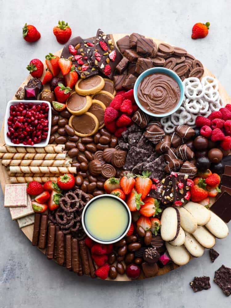This chocolate charcuterie board is a chocolate lover's dream! Enjoy a chocolatey assortment of cookies, truffles, chocolate-covered pretzels, and fruit, along with decadent sauces for dipping! Top view of chocolate charcuterie board. Berries and chocolate pieces are scattered next to the board.