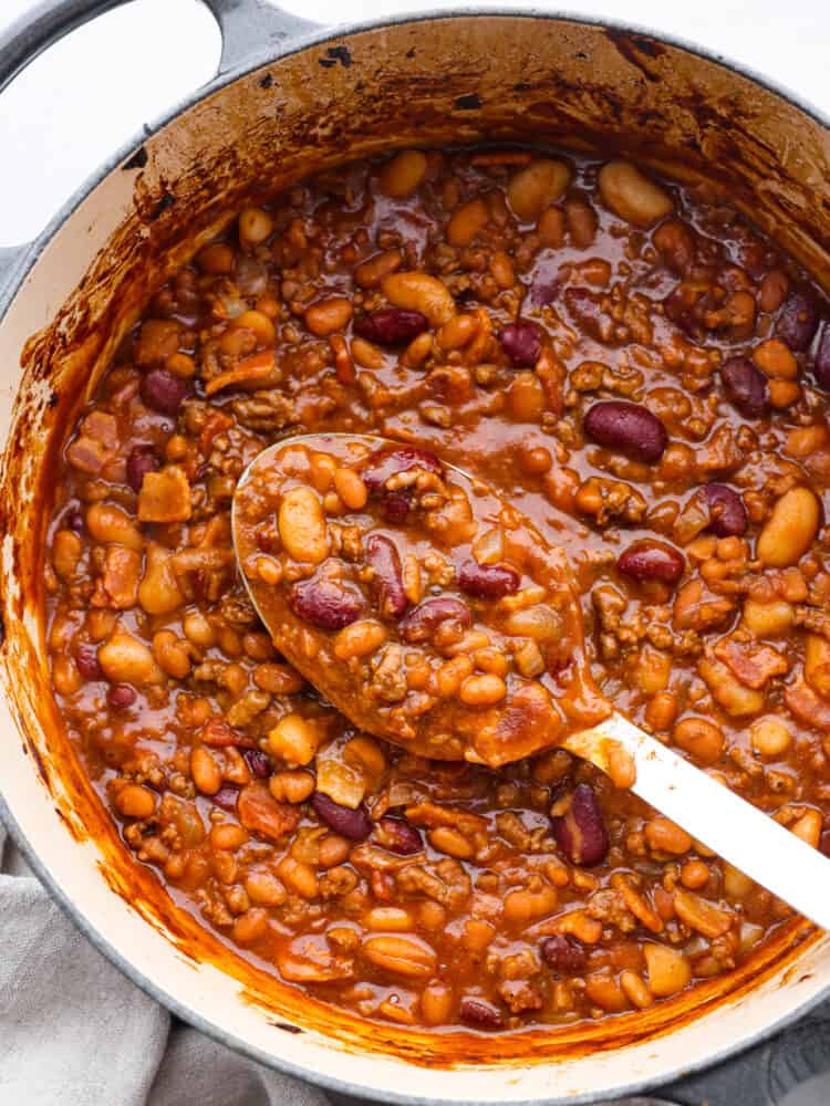 Every time I bring these cowboy beans to a summer BBQ, people start begging for the recipe, and honestly, I donโt blame them. Theyโre hearty, a little smoky, a little sweet, and always the first thing to disappear. Hero image of cowboy beans in a blue and white pot. A white serving spoon is scooping some up.