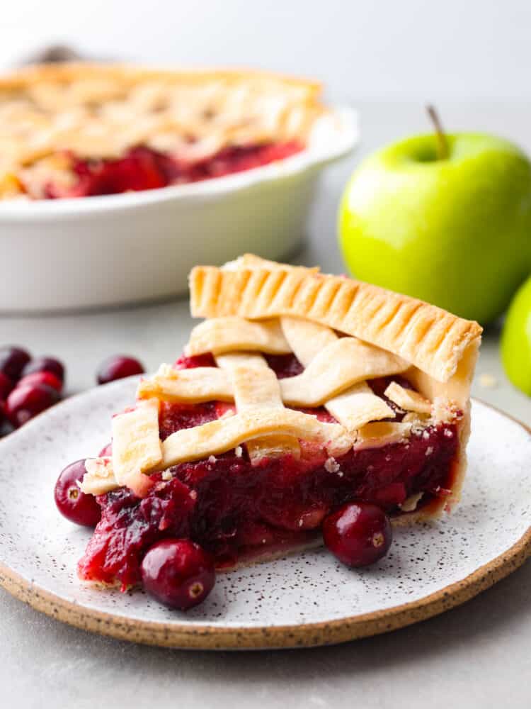 Prepare your Thanksgiving table because this cranberry apple pie is the best addition to the dinner lineup! Itโs delightfully juicy and the best combination of tart and sweet! A slice of cranberry apple pie on a stoneware plate.
