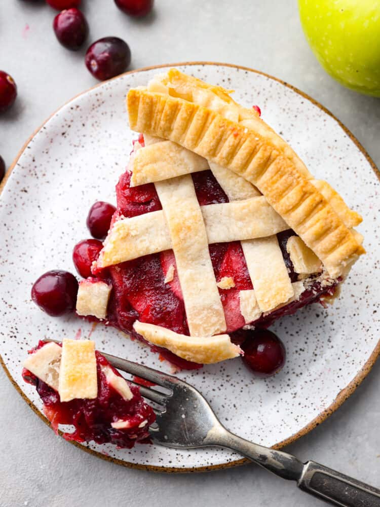 Prepare your Thanksgiving table because this cranberry apple pie is the best addition to the dinner lineup! Itโs delightfully juicy and the best combination of tart and sweet! Top-down view of a slice of pie with a bite taken out of it.