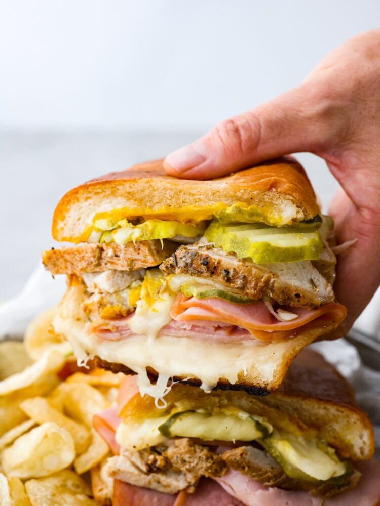 My easy Cuban sandwich is stacked with tender pork, melty Swiss, tangy pickles (my favorite), and zesty mustard! Then it's toasted in butter until perfectly crisp and golden. The close up of someone holding one half of a Cuban sandwich.