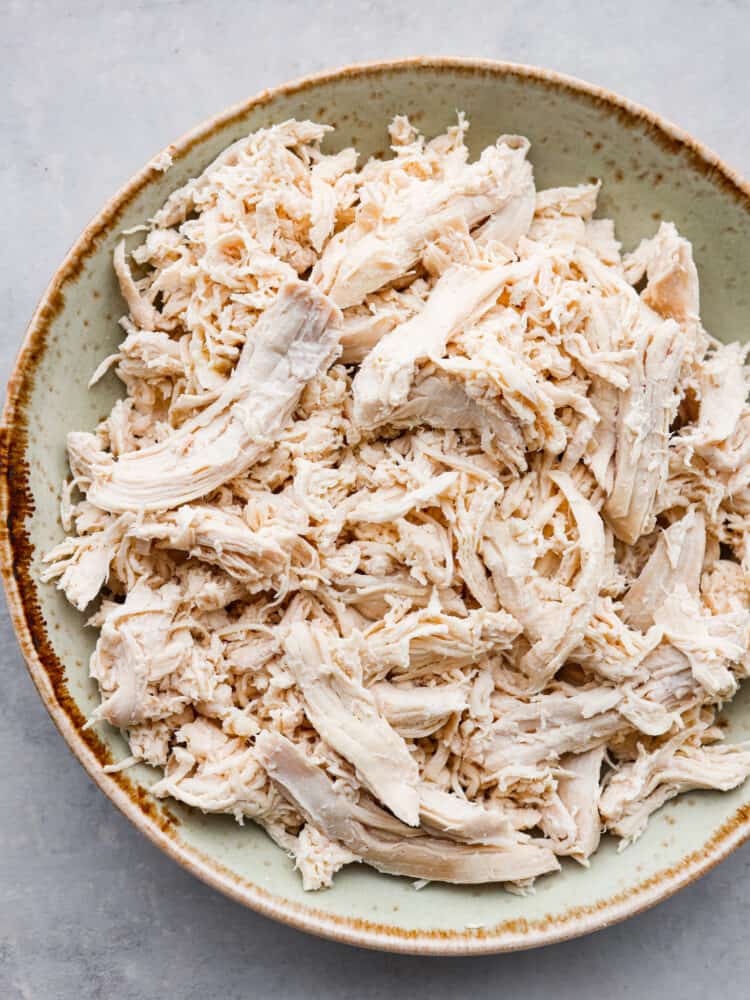 Boiled chicken makes meal prep a breeze and is the perfect way to get tender juicy chicken. This method of cooking chicken is fast and easy to shred and use in so many recipes like salads, soups, and casseroles. Close top view of shredded boiled chicken in a rustic green and brown bowl.