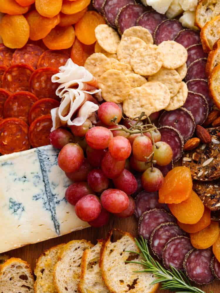 This classic Italian Charcuterie board is the perfect blend of savory and sweet. Loaded with nuts, dried fruit, cured meats, and a Caprese salad, this charcuterie board is perfect for your next get-together! A close up of the Italian charcuterie board with grapes, mangoes, cheeses, and crackers.