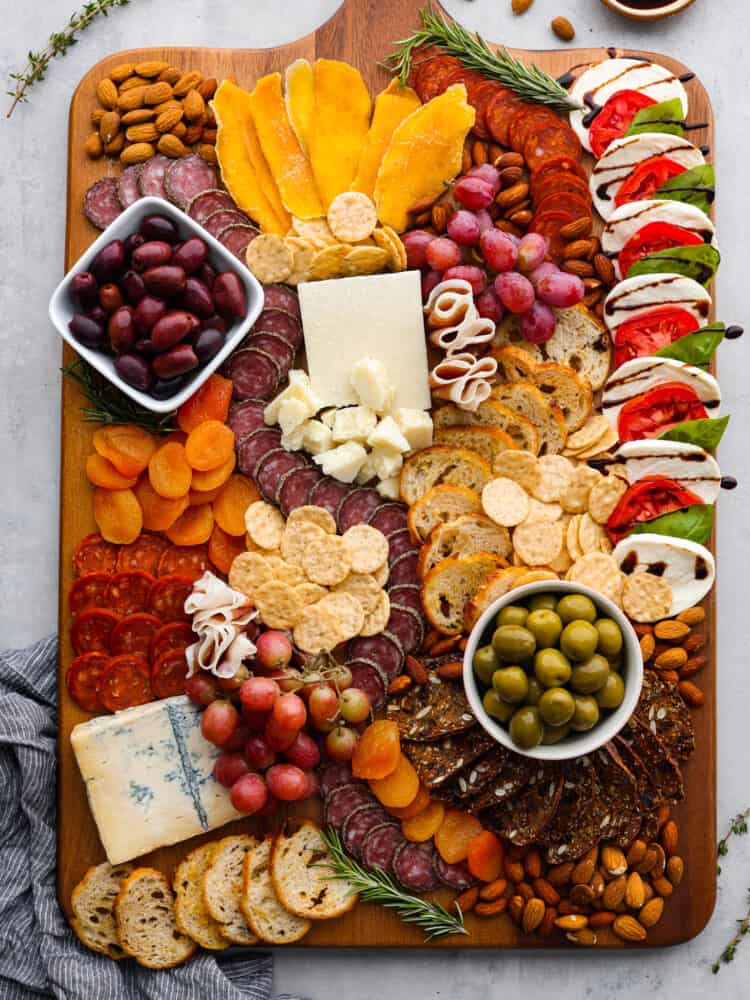 This classic Italian Charcuterie board is the perfect blend of savory and sweet. Loaded with nuts, dried fruit, cured meats, and a Caprese salad, this charcuterie board is perfect for your next get-together! An overview of the Italian charcuterie board with an assortment of meats, cheeses, nuts, and fruits.