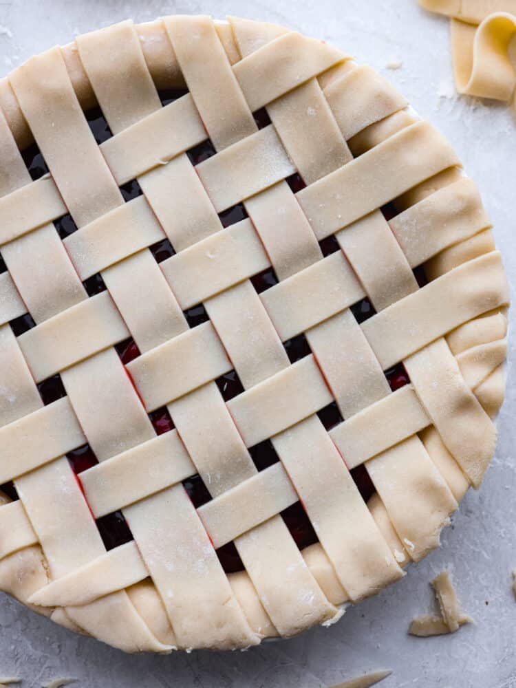A Lattice Pie Crust is visually stunning and the perfect way to finish an apple or cherry pie. This recipe will teach you how to weave strips of dough into a beautiful topper for your favorite pie, and it's easier than you think! Lattice pie crust woven on top of a cherry pie.