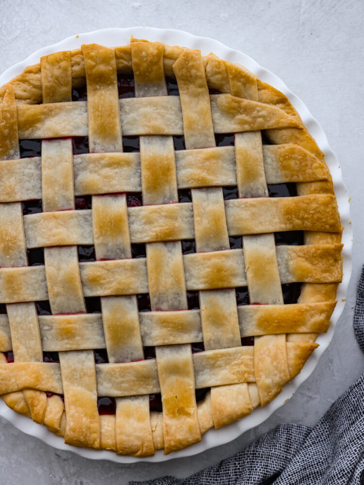 A Lattice Pie Crust is visually stunning and the perfect way to finish an apple or cherry pie. This recipe will teach you how to weave strips of dough into a beautiful topper for your favorite pie, and it's easier than you think! Lattice pie crust baked on top of a pie in a white dish.