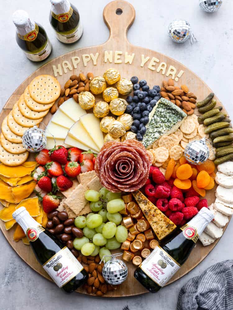 Throw a fun party and ring in the new year with this fantastic New Year's charcuterie board! Endless options of sweet and savory finger foods will keep your guests awake until midnight. Overhead view of new year's charcuterie board. Miniature sparkling ciders and disco balls surround the board.