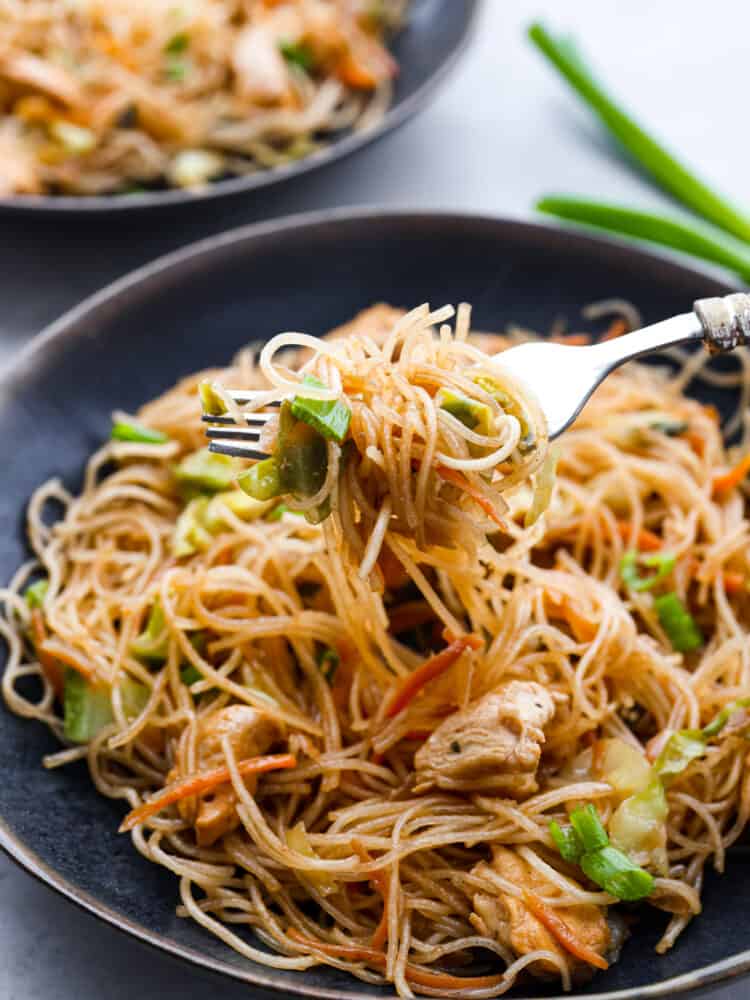 Pancit is a traditional Filipino stir-fry made with tender chicken, carrots, cabbage, and thin pancit noodles. The delicate rice noodles and savory sauce have made this meal a favorite for generations. Close up view of pancit noodles lifting out of a black bowl with a fork.