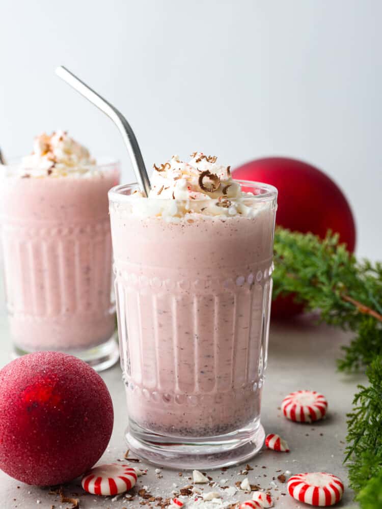 Chick-fil-A peppermint milkshakes are one of the best things about the holiday season, but they're always gone too soon! Here's how you can make this delicious peppermint shake at home with just a few simple ingredients. 2 glasses of peppermint milkshakes surrounded by red Christmas ornaments and pine tree branches.