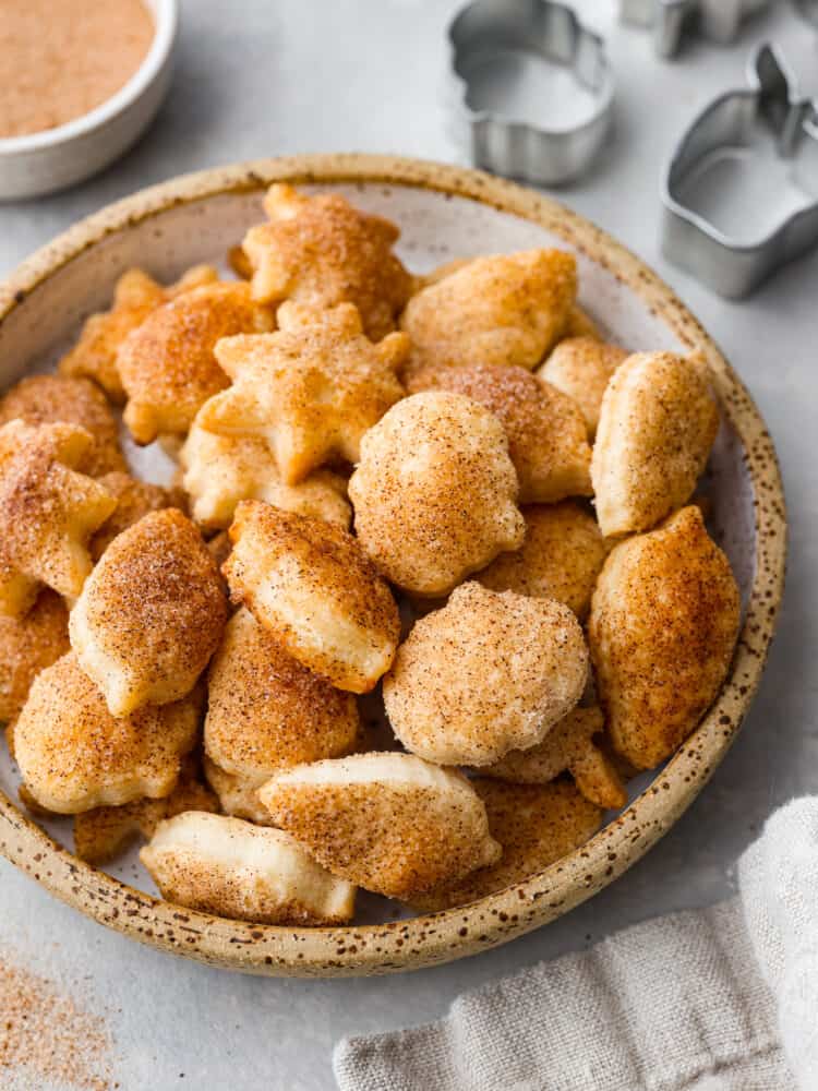 Turn leftover pie crust into perfect buttery and flakey pie crust cookies. Roll and shape using fun cookie cutters then simply sprinkle with sweet cinnamon and sugar.ย Close view of pie crust cookies on a small stone plate. Cookie cutters and cinnamon sugar are next to the plate.
