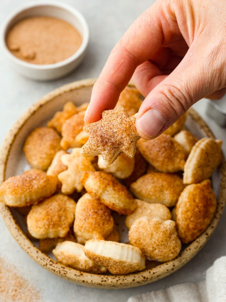 Turn leftover pie crust into perfect buttery and flakey pie crust cookies. Roll and shape using fun cookie cutters then simply sprinkle with sweet cinnamon and sugar.ย Close view of pie crust cookies on a small stone plate. A cookie is being lifted off the plate.