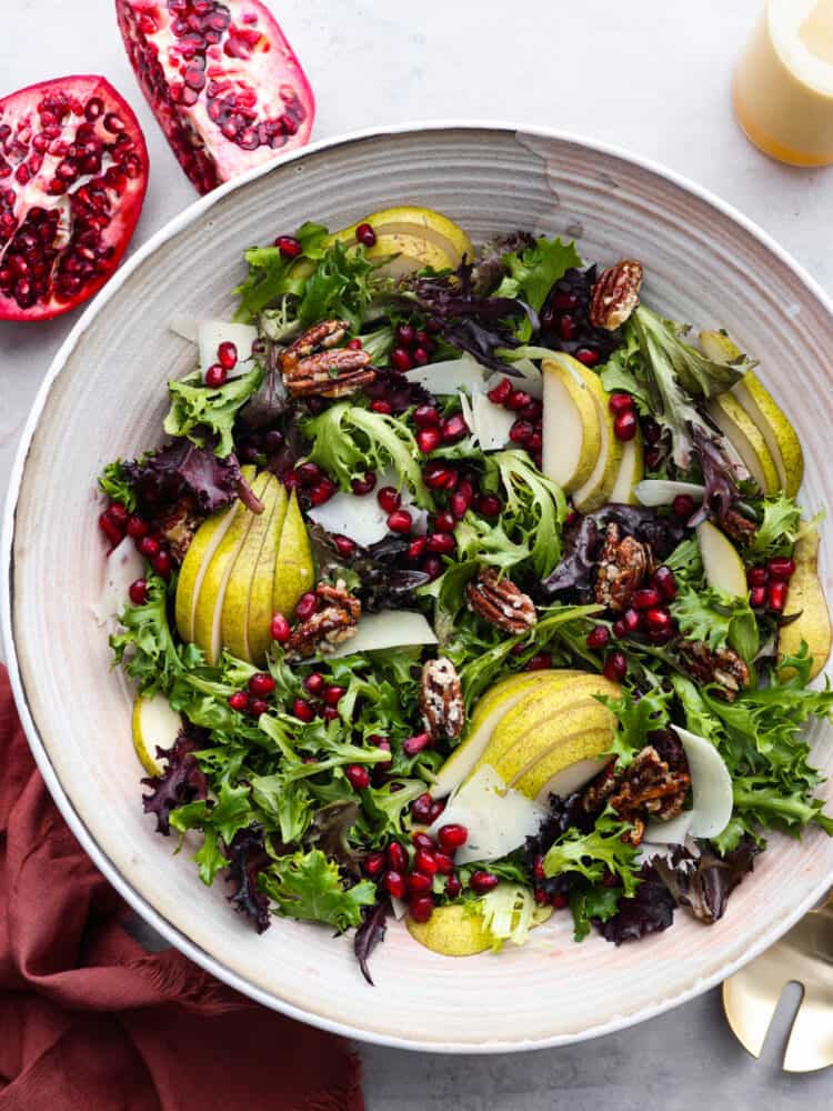 This pomegranate salad has just the right ingredients to go with any dish this holiday season! Packed with texture, different fruits, and delicious greens, you will be coming back for seconds (and probably even thirds)! The top view of a pomegranate salad in a white bowl.