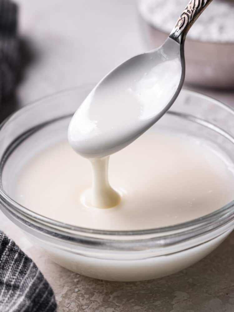 Sweet and silky Powdered Sugar Glaze is the perfect topping for your baked goods and desserts. It is so simple to make with just 3 ingredients and will be the perfect addition to your goodies! Powdered sugar glaze on a spoon and in a glass bowl.