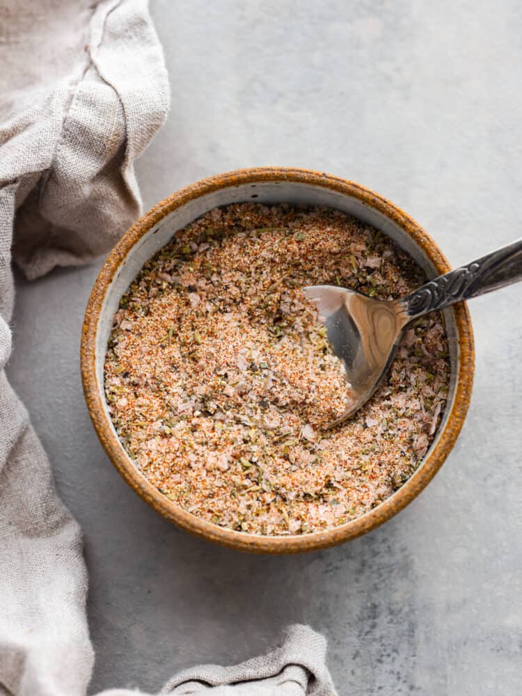 Prime Rib Rub takes 5 minutes to make and will be a staple in your spice cabinet! It is so fresh and flavorful you won't want to have your prime rib any other way. A bowl of prime rib rub with a metal spoon sticking in it.