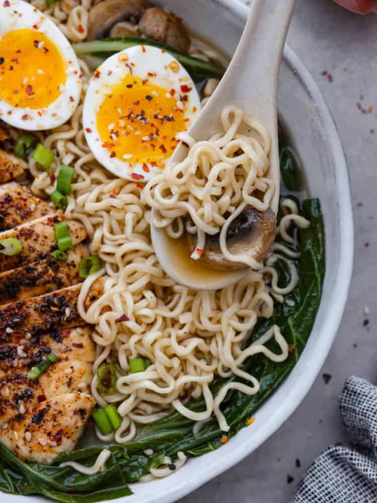 Quick and easy homemade ramen. This broth is simple to make yet bold and flavorful. Itโs perfect for pouring over some ramen noodles and loading up with your favorite toppings! This is an easy dinner that everyone will love! Closeup of ramen with noodles, a sliced mushroom, and broth in a white spoon.