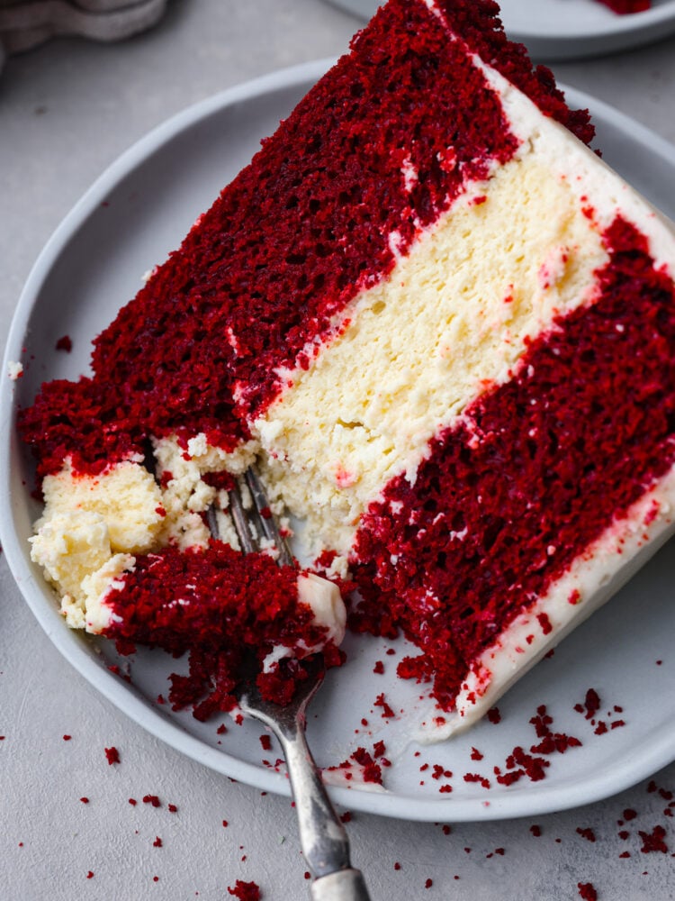 Can’t decide between red velvet cake and cheesecake? Why not both! This dreamy dessert is made with layers of moist red velvet cake and rich cheesecake topped with a luscious cream cheese frosting. Closeup of cake with a bite taken out of it.