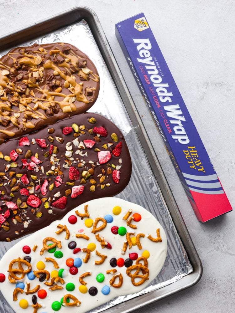 This delicious Chocolate Bark made withย Reynolds Wrapยฎ Heavy Duty Foilย will be the tastiest and simplest dessert you make all holiday season! It's quick and easy, and your entire family will go crazy over it! Finished chocolate bark on a baking sheet with Reynolds Wrap Foil box next to it.