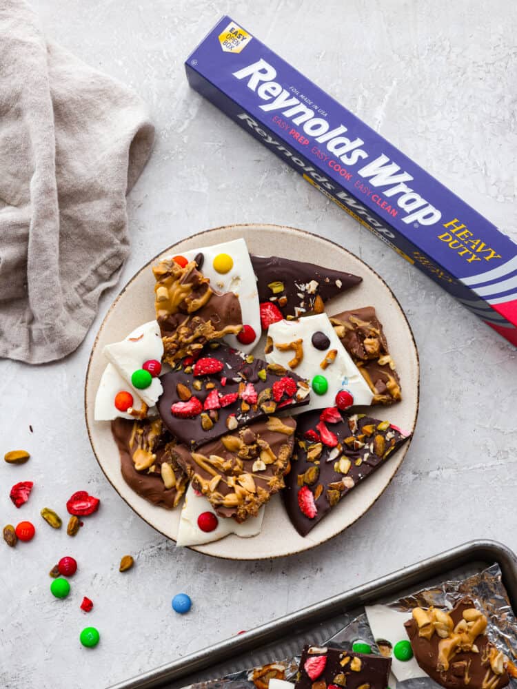 This delicious Chocolate Bark made withย Reynolds Wrapยฎ Heavy Duty Foilย will be the tastiest and simplest dessert you make all holiday season! It's quick and easy, and your entire family will go crazy over it! A plate of white chocolate bark, dark chocolate bark and milk chocolate bark with a Reynolds Wrap Foil package next to it.