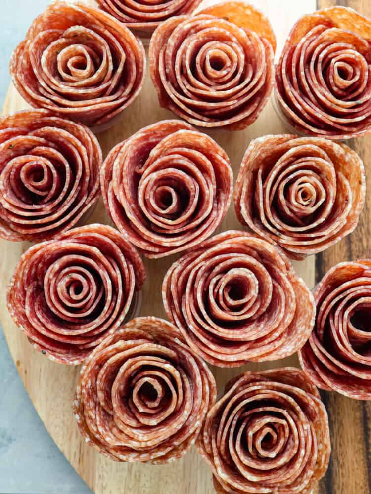 A salami rose is the perfect way to dress up your charcuterie board. This recipe will show you how to make a salami rose in two different ways that will be fun to put together and really wow your guests! A close up of the meat flowers on a wooden board.