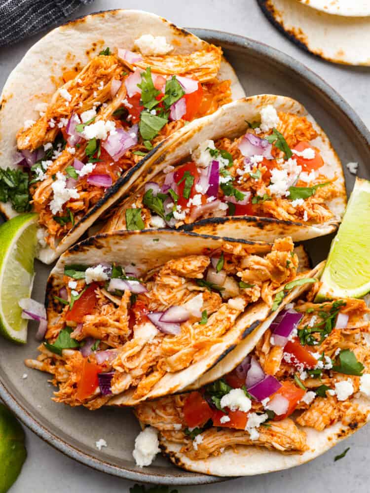 Shredded Chicken Tacos are a filling and flavorful dinner ready in just 10 minutes. The chicken is perfectly seasoned and served on a warmed tortilla topped with all of your favorite toppings. It's always a hit! Shredded chicken tacos on a black plate with limes next to them.