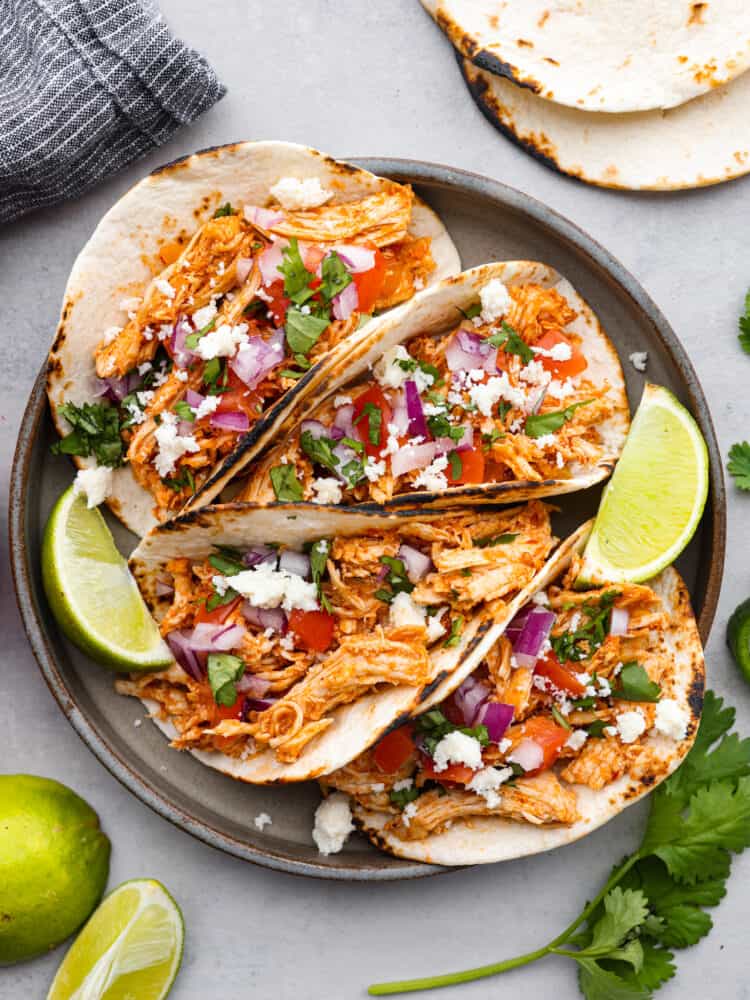 Shredded Chicken Tacos are a filling and flavorful dinner ready in just 10 minutes. The chicken is perfectly seasoned and served on a warmed tortilla topped with all of your favorite toppings. It's always a hit! Shredded chicken tacos on a plate with limes and cilantro around it.
