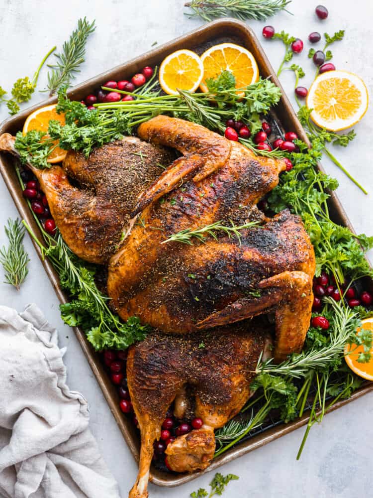 A Spatchcock Turkey cooks faster and more evenly, and will be the most tender and juicy turkey you've ever cooked! Roasted or smoked, this turkey will wow your guests come Thanksgiving day. A spatchcock turkey roasted on a pan with oranges, cranberries, and fresh herbs.